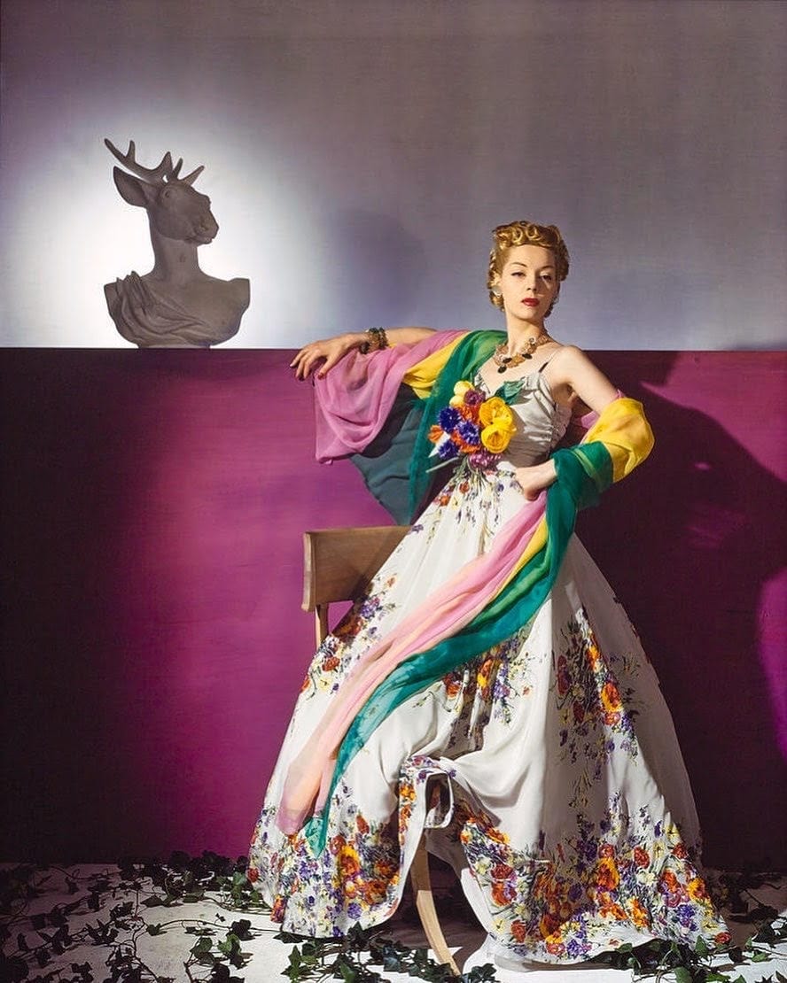 Helen Bennett dressed in a floor-length, white crepe dress printed with bright multi-colored flowers, with a large bouquet of flowers on the bodice and a long color-blocked chiffon scarf as a wrap, from the Salon Moderne at Saks Fifth Avenue, circa 1939, Courtesy of Vogue